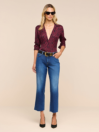 Woman wearing sunglasses, the Nina Silk Blouse in a deep red pattern, blue relaxed-fit cropped jeans, a black belt with a gold buckle, and black heels, standing against a neutral background with one hand in her pocket.