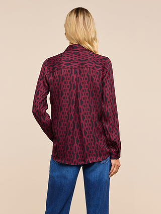 Wearing the Nina Silk Blouse—a maroon and black patterned, long-sleeve shirt in a relaxed fit—a person with long blonde hair pairs it with blue jeans, standing with their back to the camera against a plain beige background.
