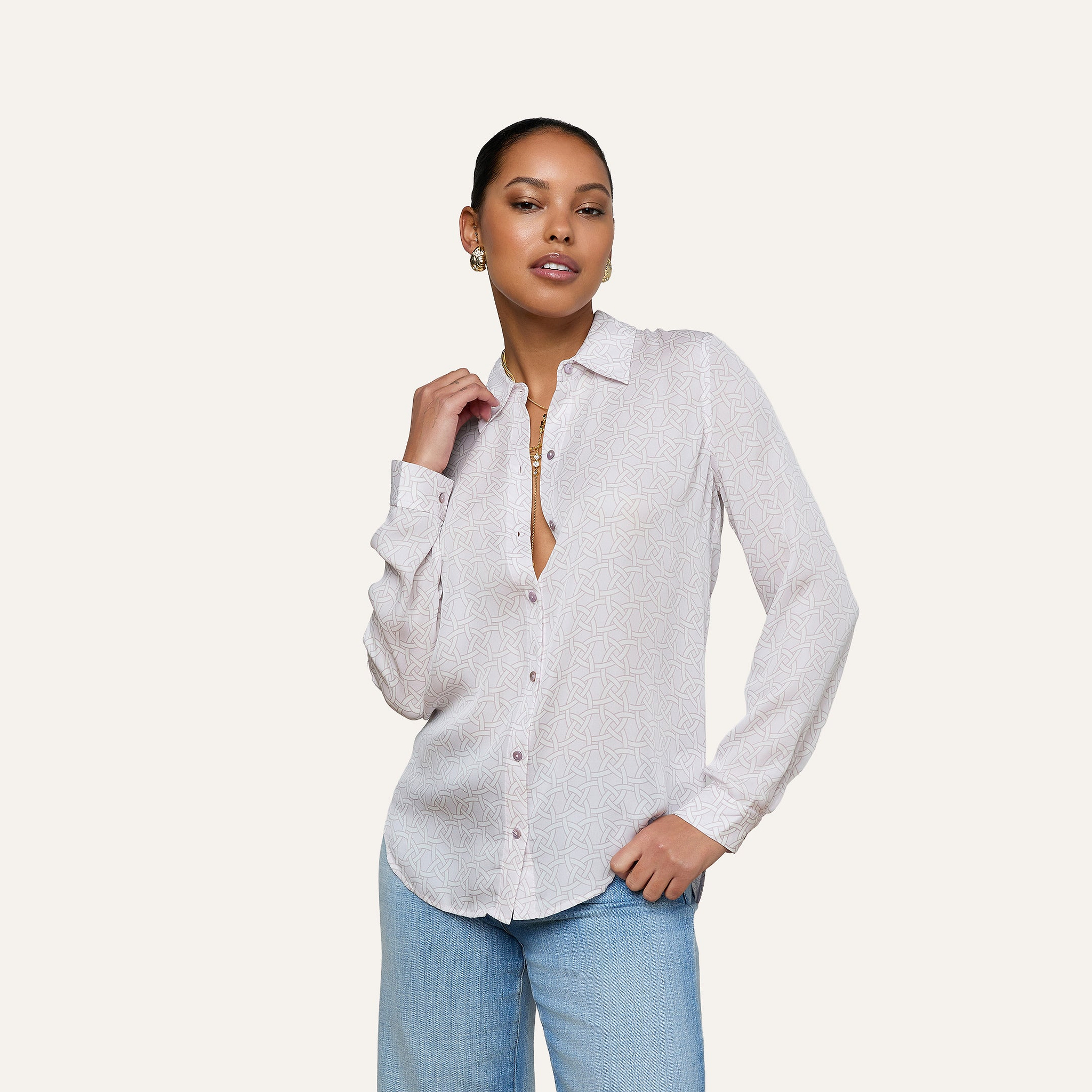 A person wearing the Nina Silk Blouse—a relaxed fit, long-sleeve silk button down shirt with a subtle geometric print—paired with light blue jeans, standing against a plain off-white background.