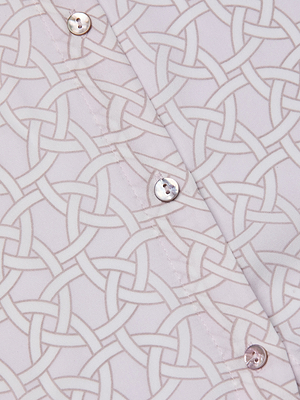 Close-up of the Nina Silk Blouse, a light-colored button down with a geometric interlocking circle print and white buttons. Visible stitching along the seams accentuates its relaxed fit.