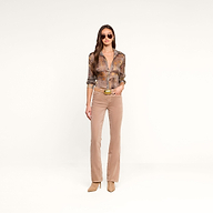 Una mujer posa frente a un fondo beige con gafas de sol, la blusa «Nina Silk» con estampado de pata de gallo marrón y corte holgado, pantalones acampanados beige con cinturón y botas de tacón. Lleva el pelo largo y castaño suelto y mira al frente con expresión neutra.
