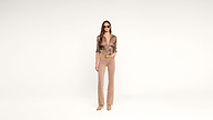 A woman wearing sunglasses, a patterned blouse, beige pants, and tan shoes stands against a plain white background with one hand in her pocket.