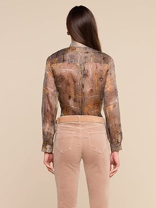 A person with long brown hair is shown from the back against a neutral background, wearing the Nina Silk Blouse—a relaxed fit sheer patterned top—paired with beige pants.