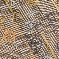 Close-up of the Nina Silk Blouse, showcasing a patterned design with vintage keys in gold, black, and gray tones. The fabric is adorned with small iridescent buttons and features a textured, woven appearance.