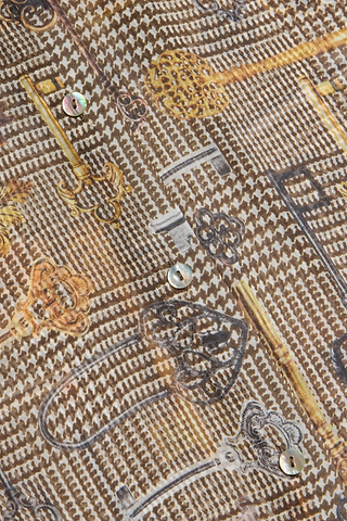 Close-up of a patterned fabric featuring vintage keys and keyholes in brown and gold tones, accented with shiny round buttons along the center. Brown houndstooth detailing subtly enhances the classic appeal, reminiscent of the relaxed fit of the Nina Silk Blouse.