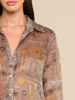 A woman wearing the Nina Silk Blouse—a relaxed fit, brown and gold button-up shirt with a collar, featuring geometric and ornate patterns. Only her lower face, neck, and upper torso are visible against a beige background.