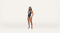 A woman stands barefoot wearing a navy and white one-piece swimsuit with a V-neck and a belt, posing against a plain white background.