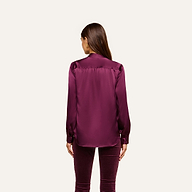 A woman with long brown hair stands facing away, wearing the Bianca Silk Blouse in purple with long sleeves and buttons, paired with matching purple velvet pants against a plain white background.