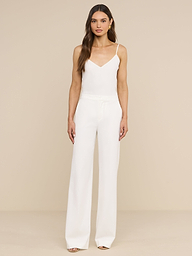 A woman stands facing forward, layering the Jane Silk Camisole with adjustable straps under a sleeveless white jumpsuit with wide-leg pants and open-toe shoes against a plain white background.