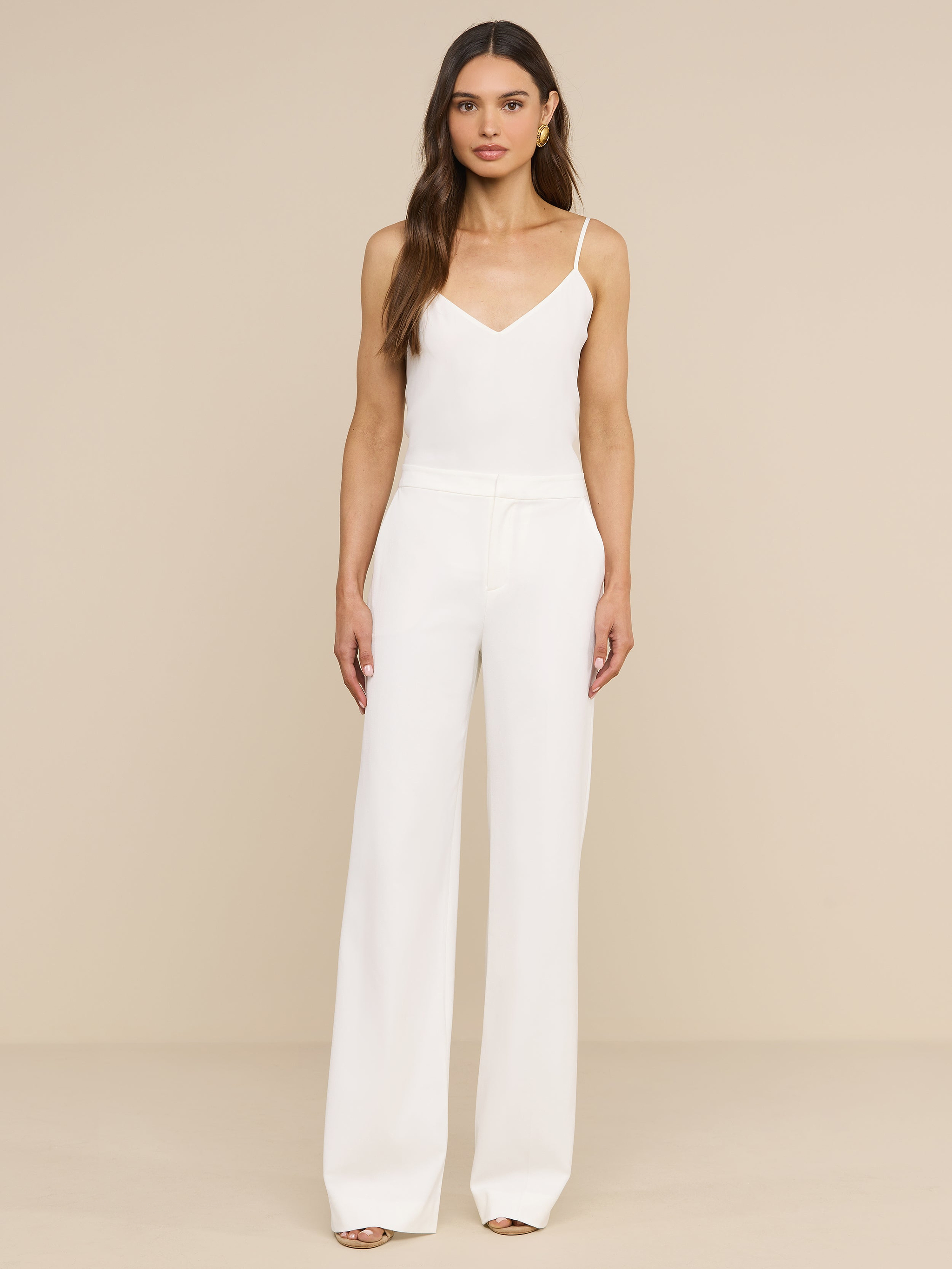 A woman stands facing forward, layering the Jane Silk Camisole with adjustable straps under a sleeveless white jumpsuit with wide-leg pants and open-toe shoes against a plain white background.