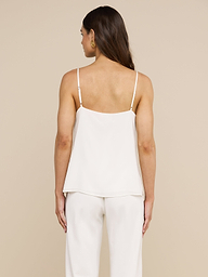 A woman with long brown hair stands facing away, wearing the Jane Silk Camisole with adjustable straps and matching white pants, set against a plain light background.