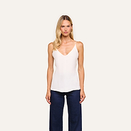 A woman with long blonde hair wears the Gabriella Silk Camisole in ivory with adjustable straps and dark blue pants, standing against a plain light background.