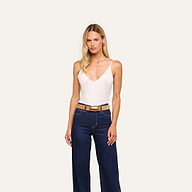 A woman with long blonde hair wears the Gabriella Silk Camisole in ivory, paired with high-waisted dark blue jeans and a tan belt, standing against a plain light background.