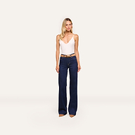 A woman faces forward wearing the Gabriella Silk Camisole in ivory with adjustable straps, paired with dark blue high-waisted wide-leg jeans, a brown belt, and brown pointed shoes against a plain light background.
