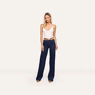 A woman wears the Gabriella Silk Camisole with adjustable straps, dark blue high-waisted wide-leg jeans, and brown shoes, standing against a plain light background.