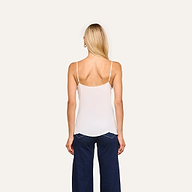 A woman with long blonde hair wears the Gabriella Silk Camisole with adjustable straps and dark blue wide-leg jeans, standing facing away from the camera against a plain, light background.