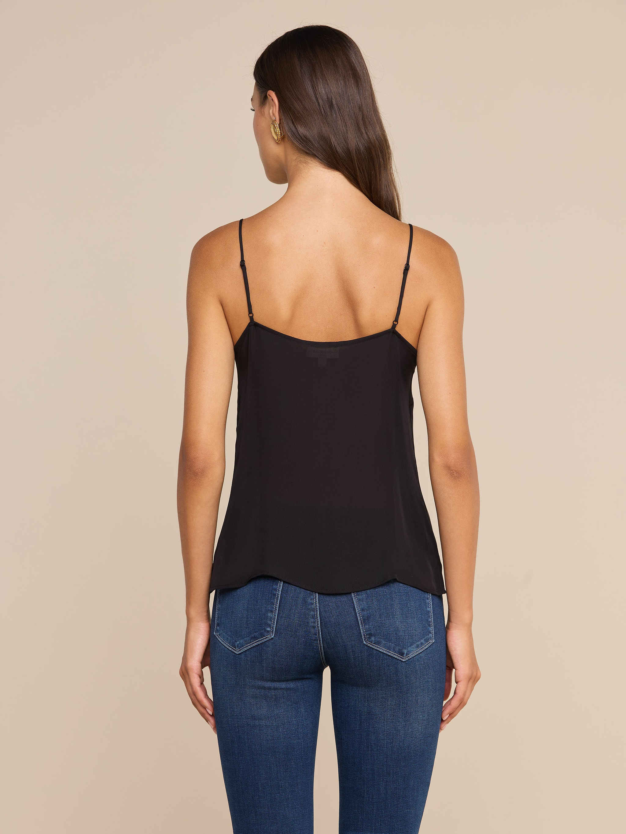 A woman faces away, wearing the Gabriella Silk Camisole in black and blue jeans, standing against a plain light background.
