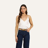 Una donna dai lunghi capelli castani indossa la canotta in seta Gabriella color avorio, abbinata a jeans a vita alta blu scuro e a una cintura marrone con fibbia dorata: un capo indispensabile per creare look a strati in qualsiasi guardaroba.