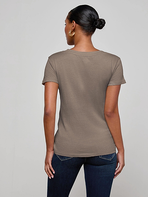 A woman with her hair in a bun and large hoop earrings wears the L'AGENCE Cory Cotton Scoopneck Tee in taupe and dark jeans, standing with her back to the camera against a plain light background.