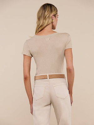 A woman with blonde hair stands facing away, wearing the Cory Cotton Scoopneck Tee in taupe and high-waisted light jeans with a brown belt, set against a neutral background.