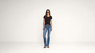 A woman wearing sunglasses, a black t-shirt, blue jeans, and black heeled sandals stands against a plain white background.