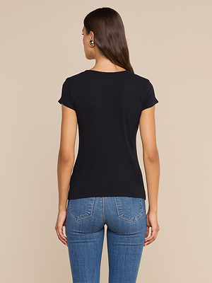 Eine Frau mit langen braunen Haaren, die ein schwarzes Cory Cotton-T-Shirt mit Rundhalsausschnitt und eine blaue Jeans trägt, steht mit dem Rücken zur Kamera vor einem beigen Hintergrund.