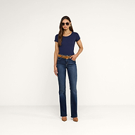 Una donna è in piedi su uno sfondo beige e indossa occhiali da sole, la maglietta Cory Cotton Scoopneck Tee in blu navy, jeans blu con una cintura marrone, tacchi alti color cuoio e ha i capelli lunghi e lisci. Ha le mani appoggiate con disinvoltura nelle tasche anteriori.