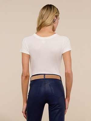 A person with long blonde hair, wearing the Cory Cotton Scoopneck Tee in vintage off-white and dark blue pants, stands facing away from the camera against a plain beige background.