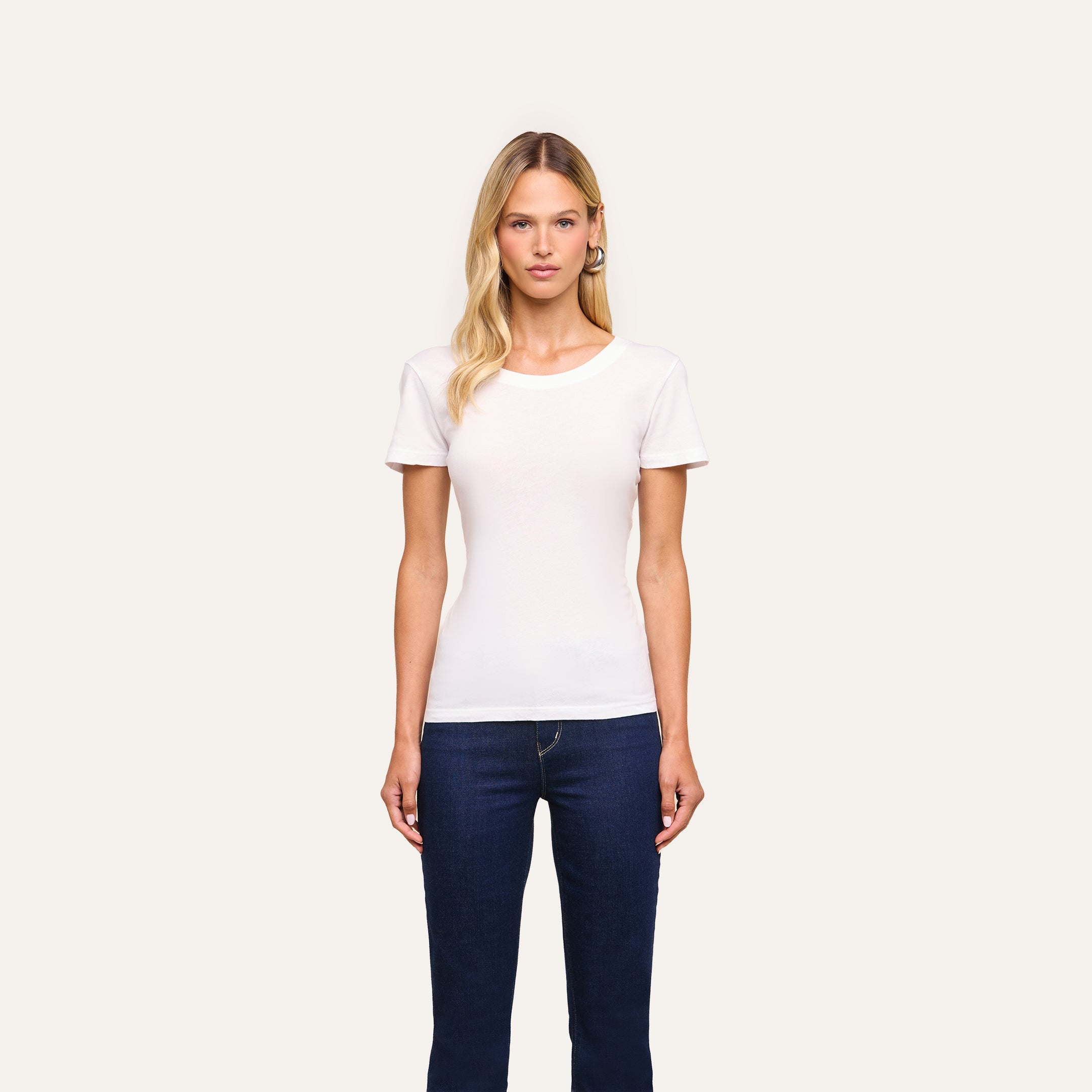 A woman with long blonde hair faces forward, wearing the Cory Cotton Scoopneck Tee in classic white and dark blue jeans, set against a light background.