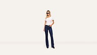 A stylish woman in sunglasses, a white T-shirt, and blue jeans stands confidently against a plain white background.