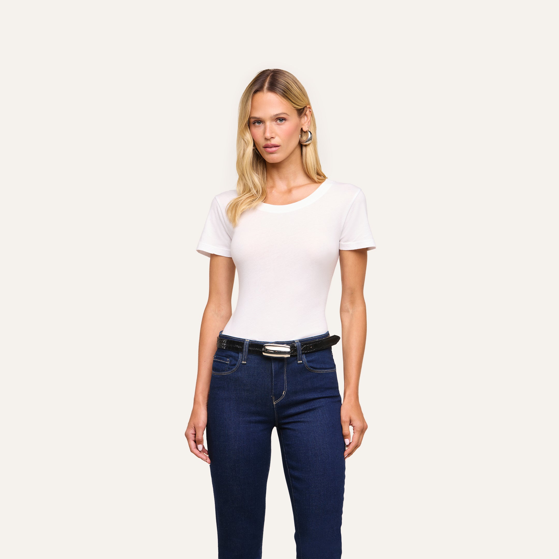 A woman faces forward, wearing the Cory Cotton Scoopneck Tee, dark blue jeans, and a black belt against a plain light background.