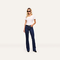 Woman wearing black sunglasses, the Cory Cotton Scoopneck Tee, dark blue bootcut jeans, and black shoes stands against a plain light background with her left hand in her pocket.