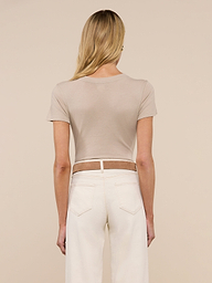 Woman with long brown hair stands with her back to the camera, wearing the Becca Cotton V-Neck Tee in beige and off-white jeans against a neutral background.
