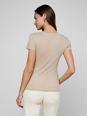 Woman with long brown hair stands with her back to the camera, wearing the Becca Cotton V-Neck Tee in beige and off-white jeans against a neutral background.
