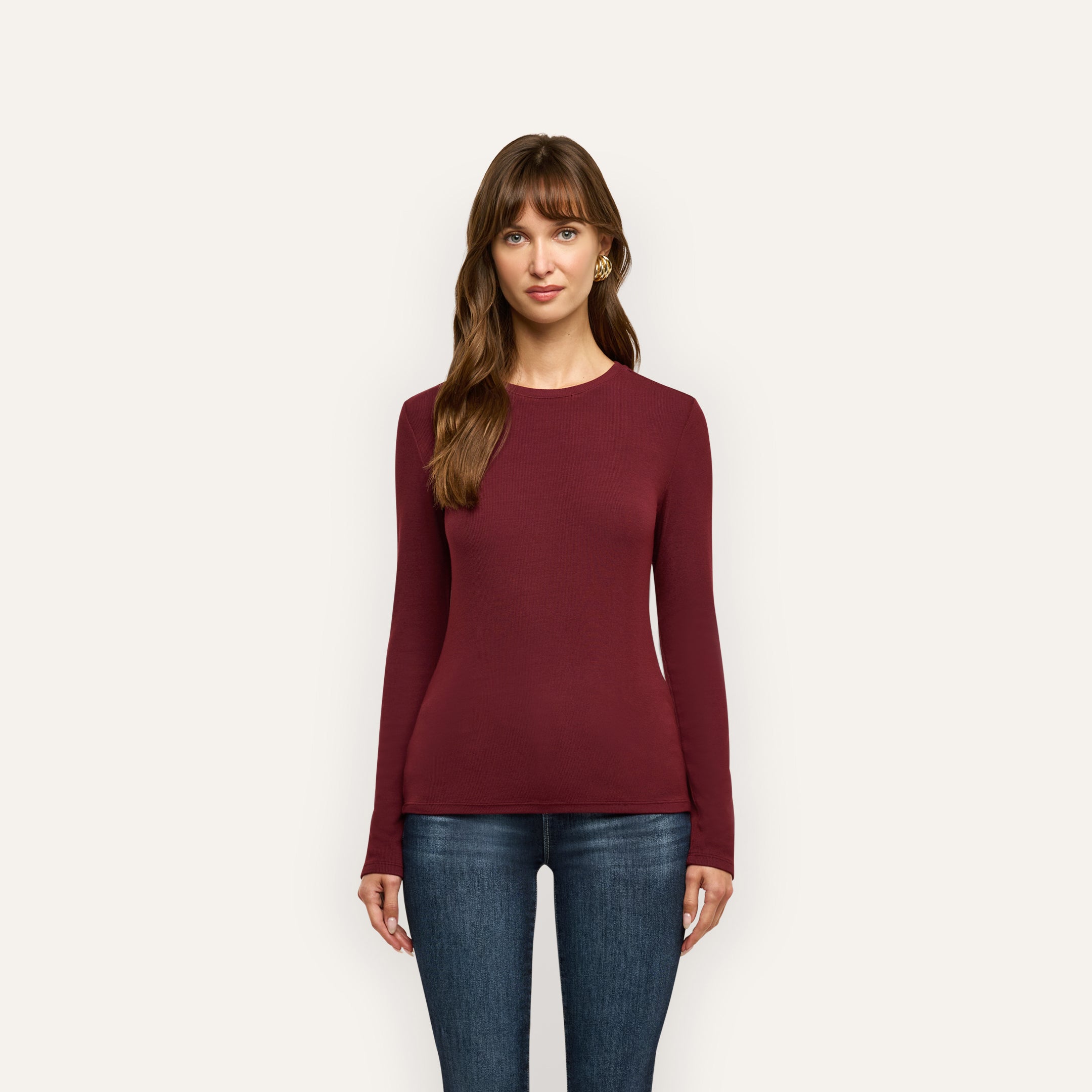 A woman wearing a slim fit, long-sleeved burgundy Tess Long Sleeve Tee and dark blue jeans.