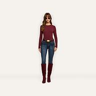 A woman wearing a maroon Tess Long Sleeve Tee, dark wash jeans with a large gold-buckled belt, and knee-high maroon suede boots.