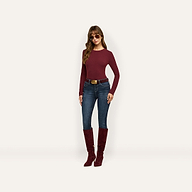A woman wearing a maroon Tess Long Sleeve Tee, dark-wash jeans with a brown belt, and matching maroon knee-high boots, accessorized with sunglasses.