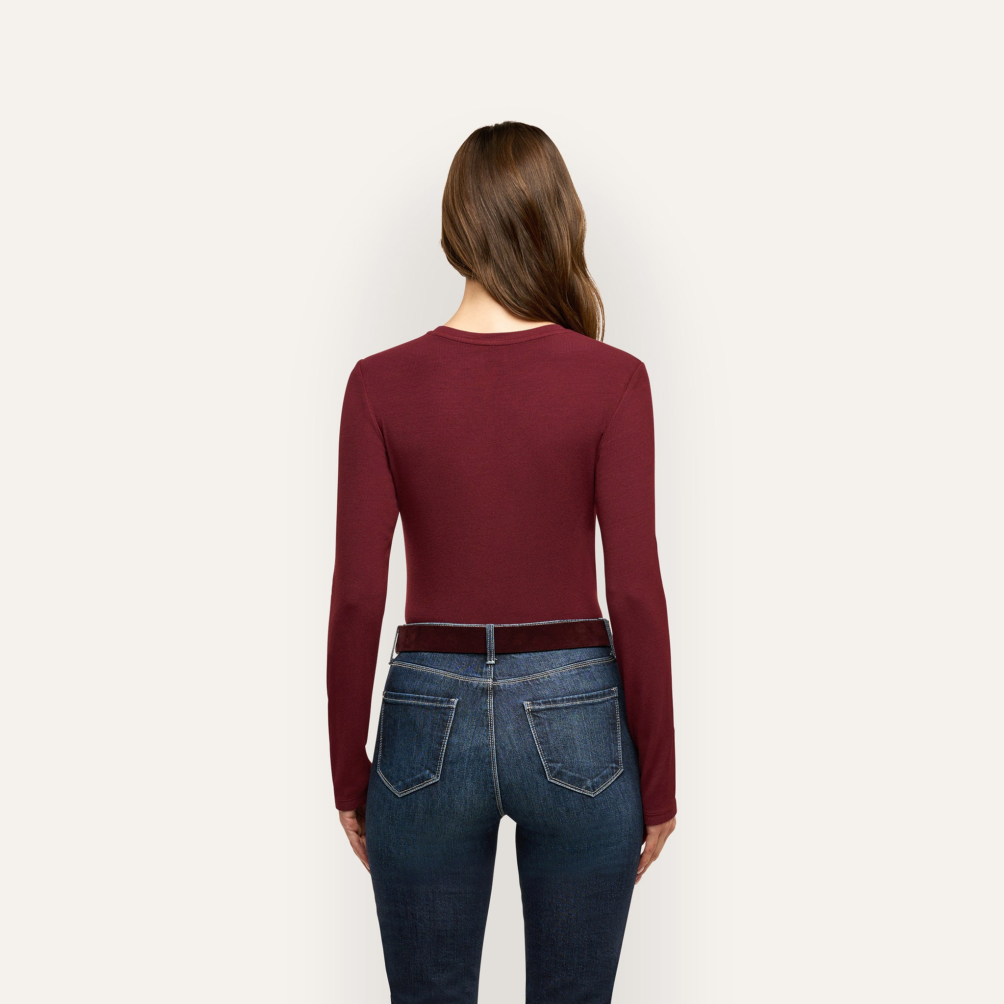 Back view of a person wearing a slim fit, burgundy Tess Long Sleeve Tee tucked into dark blue jeans with a belt.