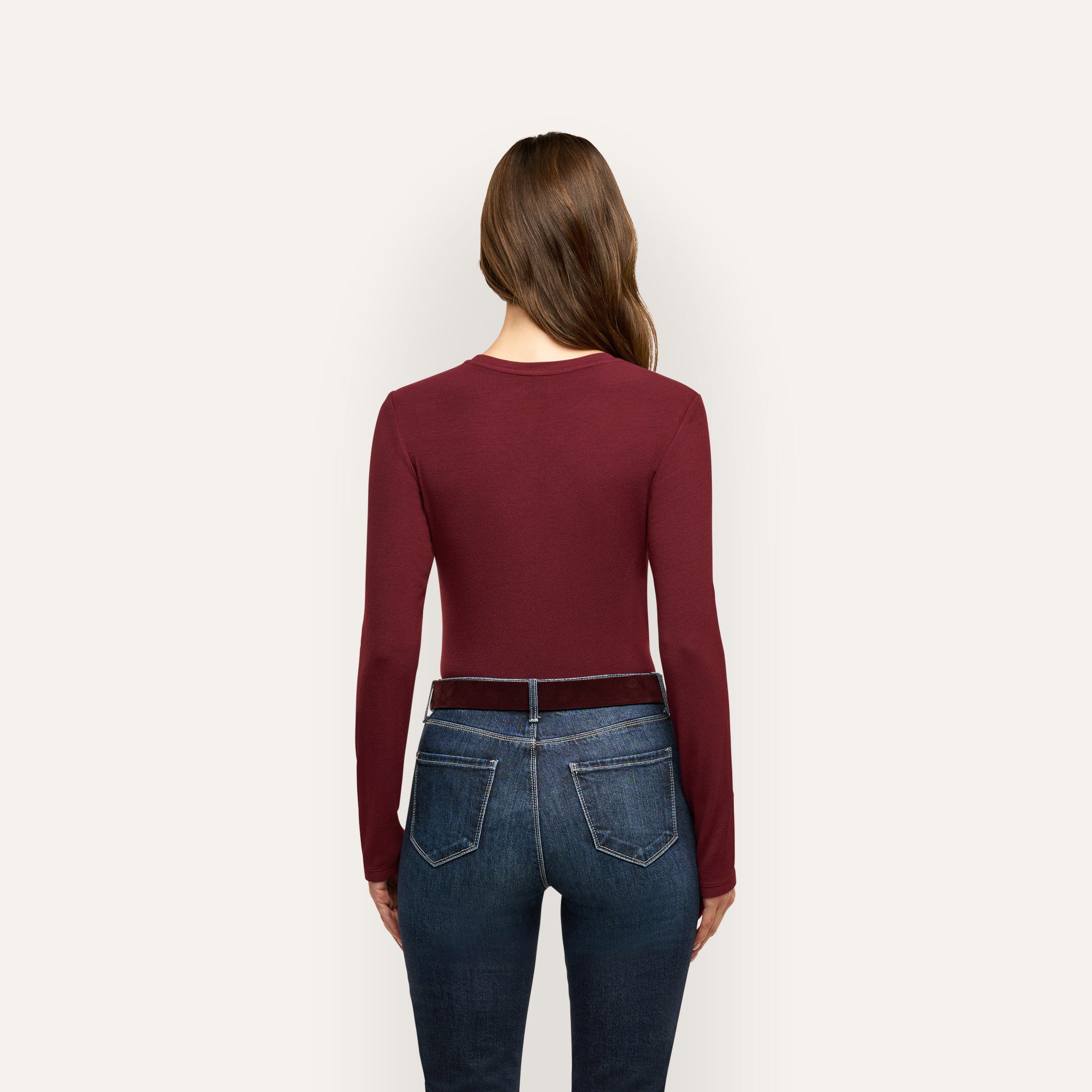 Back view of a person wearing a slim fit, burgundy Tess Long Sleeve Tee tucked into dark blue jeans with a belt.