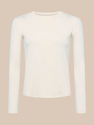 The Tess Long Sleeve Tee, a slim fit cream top made from soft rayon jersey, is displayed against a beige background.