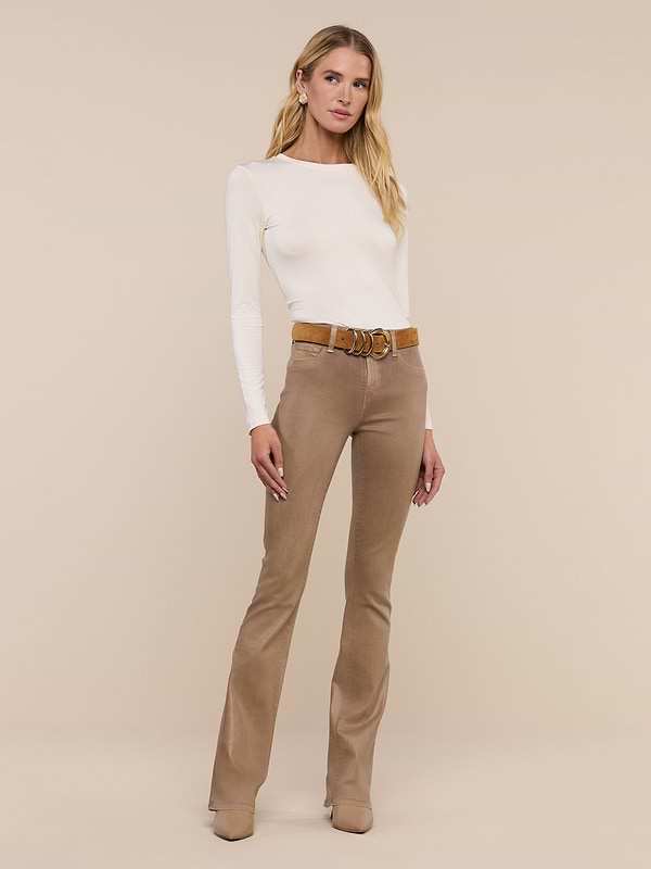 A woman with long blonde hair stands against a plain white background, wearing the Tess Long Sleeve Tee in a slim fit, paired with tan flared pants, a brown belt, and tan boots as she looks at the camera.