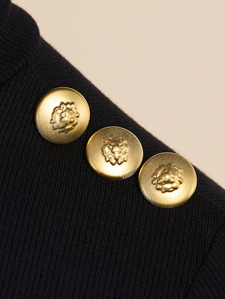 Close-up of three gold embossed lion head buttons arranged in a row on the black ribbed fabric of the Aja Turtleneck.