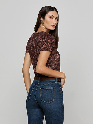 A woman wearing the L'AGENCE Ressi Fitted Tee with a brown paisley print and blue jeans stands facing away, looking over her shoulder with one hand in her pocket against a plain light background.