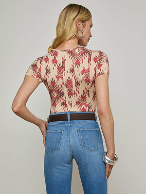 A woman with wavy blonde hair, shown from the back against a plain background, wears the Ressi Fitted Tee with geometric print, light blue jeans, hoop earrings, and silver bangles.