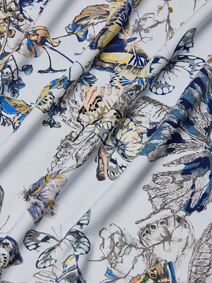 A close-up of stretch jersey fabric with a colorful butterfly print in blue, yellow, and beige on a light background. The softly folded fabric highlights the texture and pattern, perfect for the Ressi Fitted Tee.