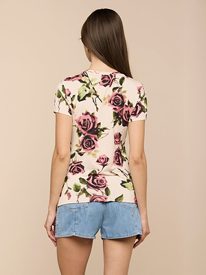 A woman with long brown hair is shown from the back, wearing the Ressi Fitted Tee with a pink and purple floral print and light blue denim shorts, standing against a plain beige background.