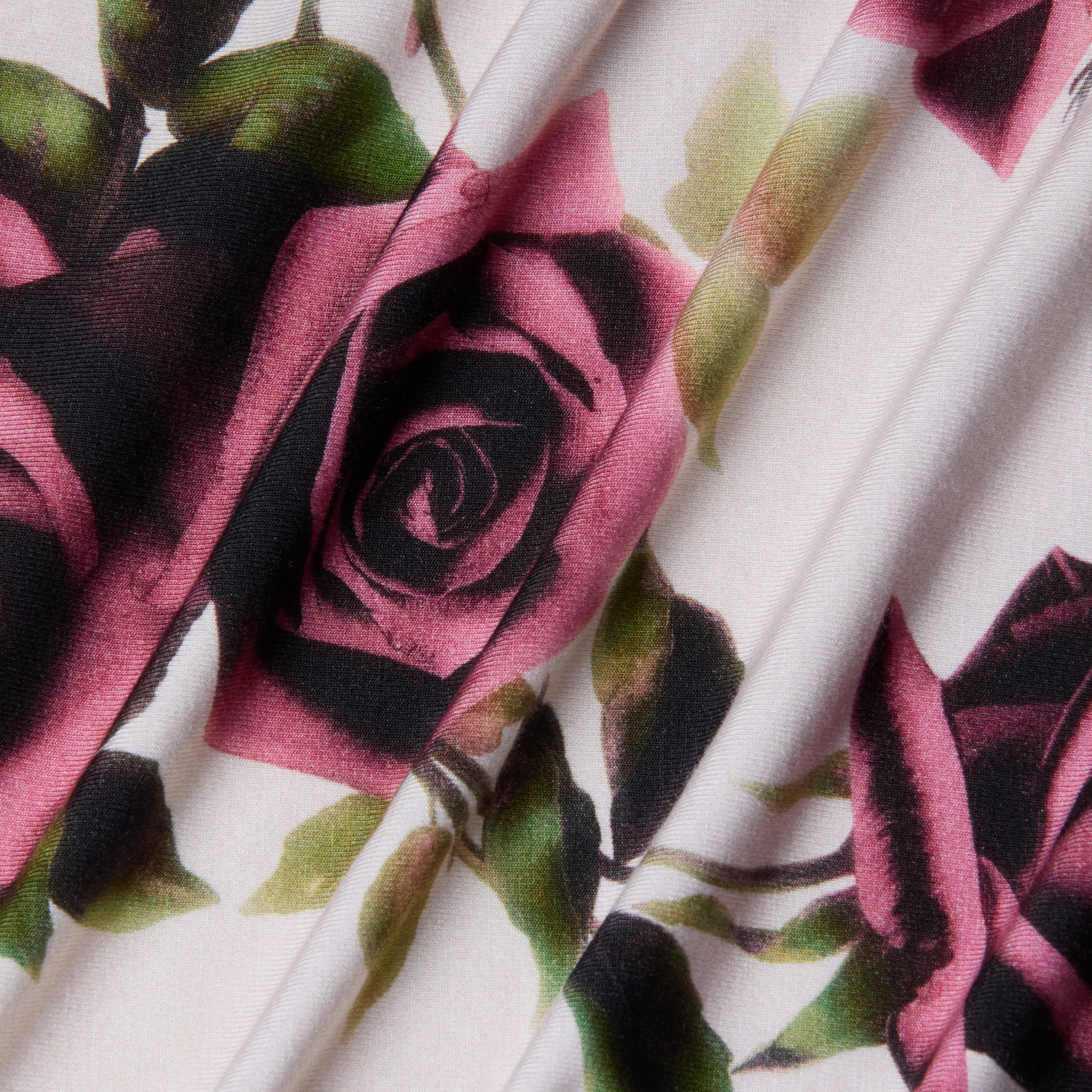 Close-up of the Ressi Fitted Tee’s stretch jersey knit fabric, featuring a printed pattern of pink and dark roses with green leaves on a light background, shown with soft folds that create subtle shadows and texture.