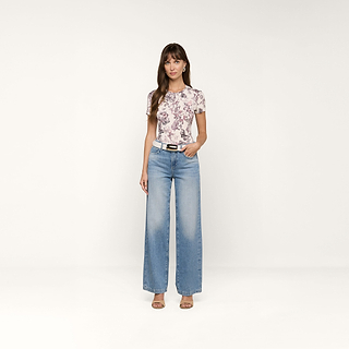 Eine Frau mit langen braunen Haaren und einem neutralen Gesichtsausdruck steht vor einem beigen Hintergrund und trägt das Ressi Fitted Tee, hellblaue Jeans mit weitem Bein, einen weißen Gürtel und beigefarbene Sandalen mit Absatz.