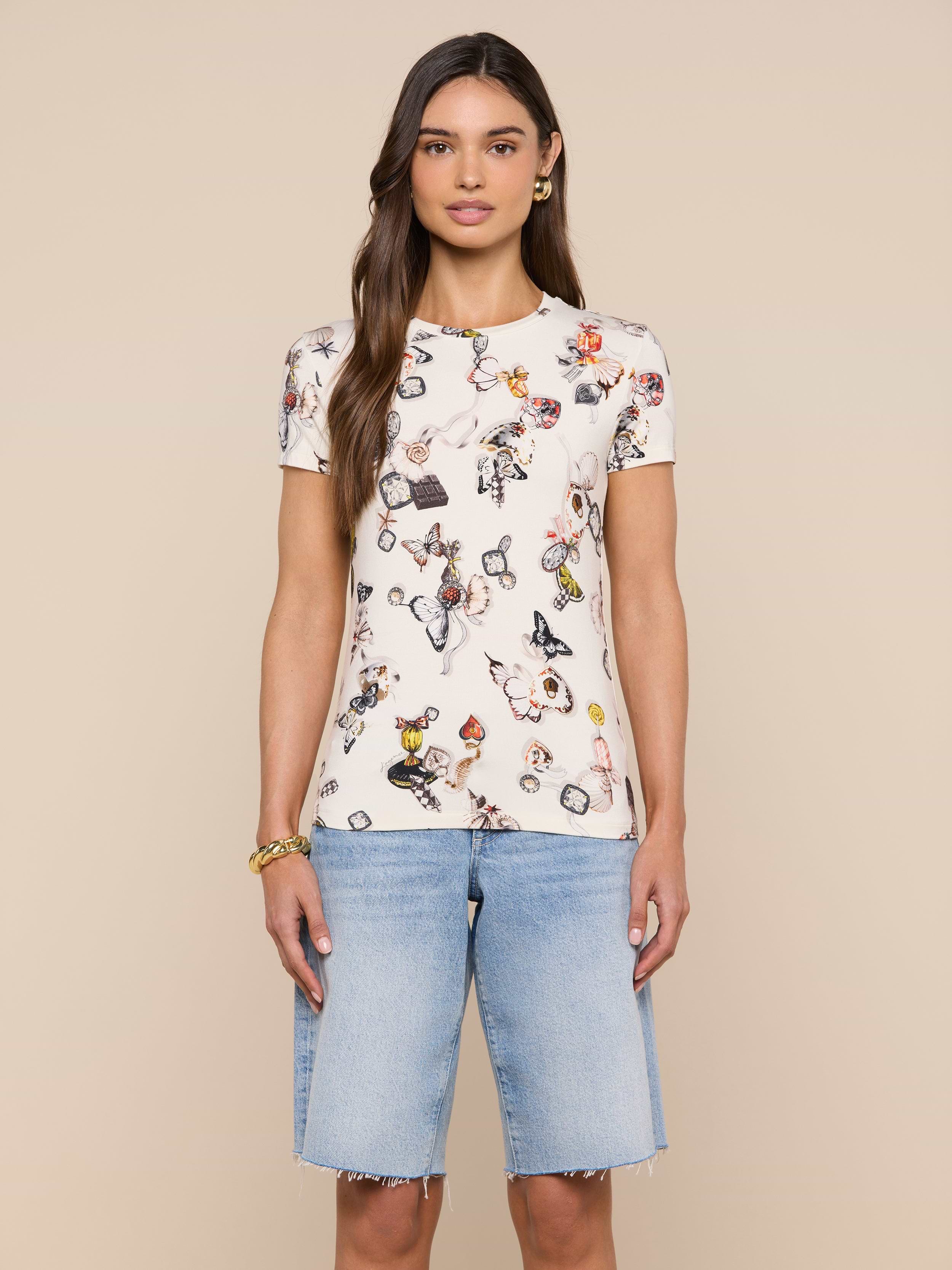 Wearing the Ressi Fitted Tee—a bestselling white T-shirt featuring a colorful print and crafted from slim-cut, stretch jersey knit—a woman stands facing forward against a plain, light background, paired with light blue knee-length denim shorts.