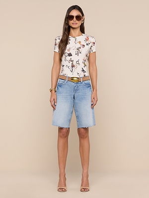 Woman stands against a beige background wearing sunglasses, the bestselling Ressi Fitted Tee in soft stretch jersey knit, light blue knee-length denim shorts, a brown belt, nude heels, and gold bracelets.